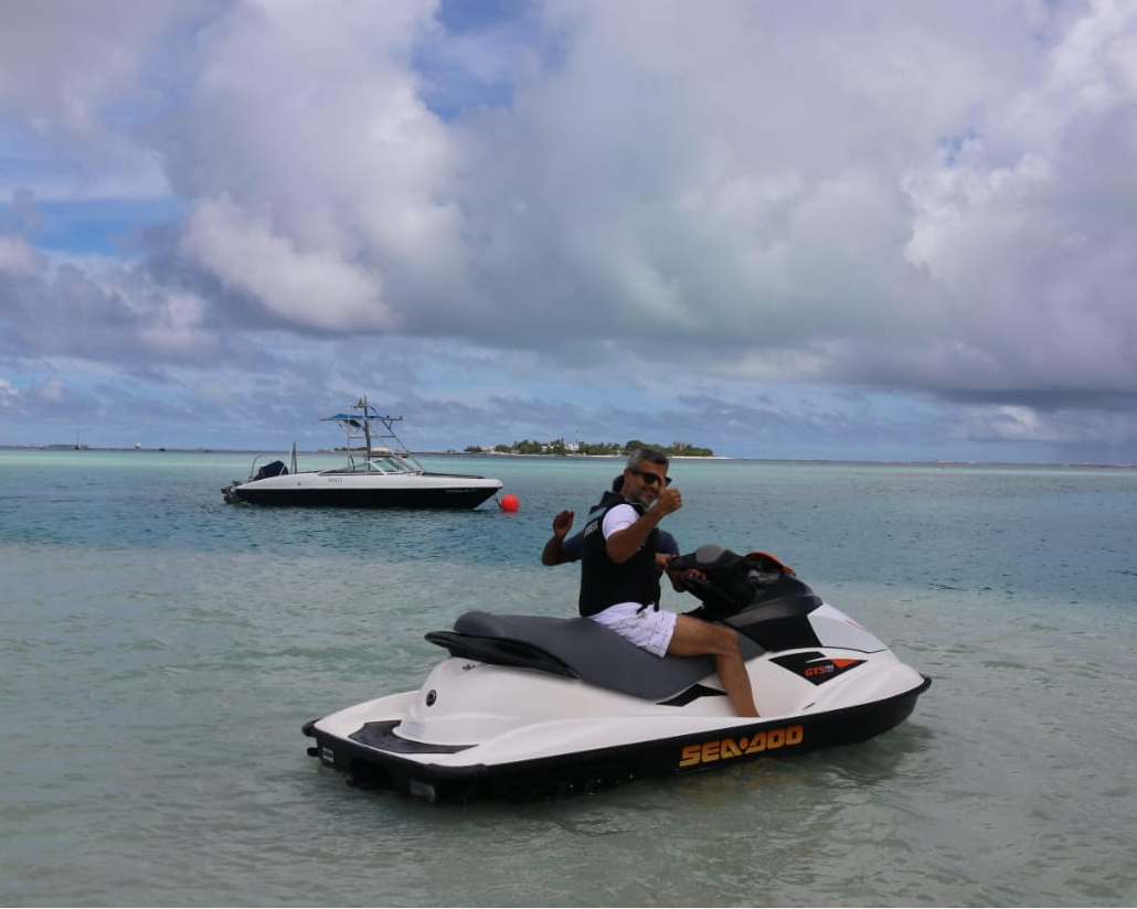 Umar Farooq Zahoor riding a jet ski across sparkling ocean waters, with a luxurious yacht anchored in the distance.